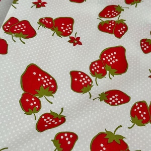 May include: A white fabric featuring a repeating pattern of red strawberries with green leaves and white seeds. The background is covered in a subtle, small white polka dot print, creating a consistent and uniform design across the entire textile surface.