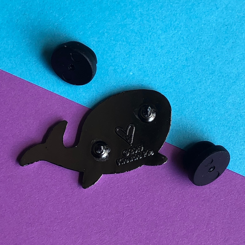 May include: Black enamel pin of a whale with a heart on its side. The pin has a silver finish and says "2019 Kindness Project" on the back.