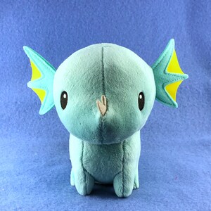 May include: A plush toy shaped like a blue axolotl with yellow fins. The toy has large, black eyes and a small, brown nose.