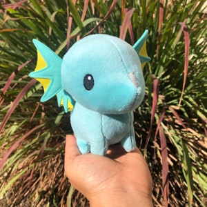 May include: A light blue plush toy with yellow fins and large black eyes. The toy is shaped like a small, cartoonish sea creature.