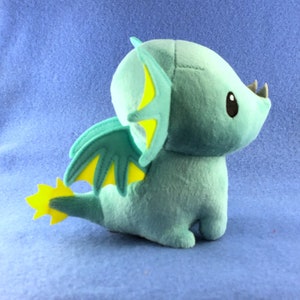 May include: A plush toy dragon with a light blue body, yellow wings, and a yellow tail. The dragon has a cute, cartoon-like face with large eyes.