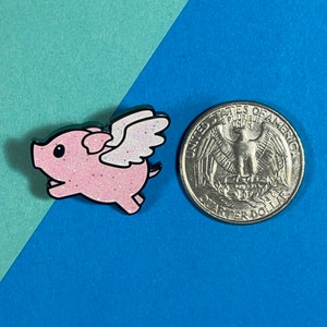 May include: A pink glitter pig with white wings flying, next to a US quarter for size comparison.