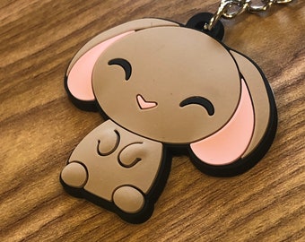 May include: A brown and pink rubber keychain shaped like a cartoon bunny with a heart-shaped nose and smiling eyes.