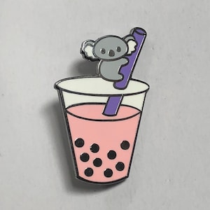 May include: A pink and white enamel pin of a boba tea with a grey koala holding onto a purple straw.