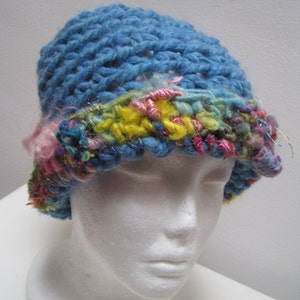 May include: A blue crochet hat with a colorful brim. The hat is made of thick yarn and features a textured stitch pattern. The brim is adorned with pink, yellow, and blue yarn, creating a vibrant contrast.