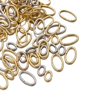May include: A pile of oval-shaped metal jump rings in gold and silver tones. The rings are scattered on a white background.