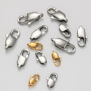 May include: A collection of silver and gold lobster claw clasps. The clasps vary in size and design, with a polished, metallic appearance. These clasps are often used in jewellery making and other craft projects.