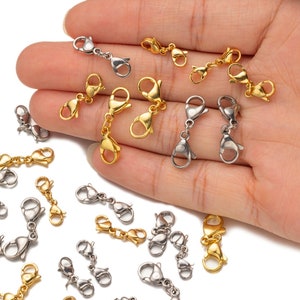 Op de afbeelding: Een verzameling gouden en zilveren karabijnhaken, die vaak worden gebruikt voor het maken van sieraden. De karabijnhaken worden getoond op een hand, waarbij sommige karabijnhaken met elkaar zijn verbonden om kettingen te vormen.