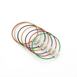 May include: Set of seven colorful key rings made of braided metal cable with silver metal clasps.