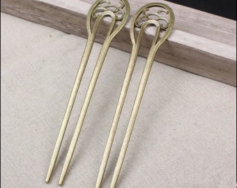 Puede incluir: Dos palos para el pelo de color dorado con tapas decorativas, ornamentadas y con forma de flor. Los palos son largos y delgados.