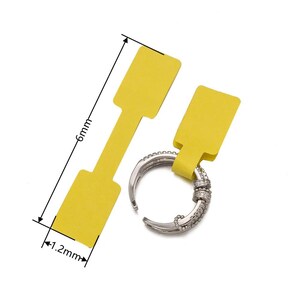 May include: Two yellow paper price tags with a 1.2 inch by 6 inch size. The tags are attached to a silver ring with small clear stones.