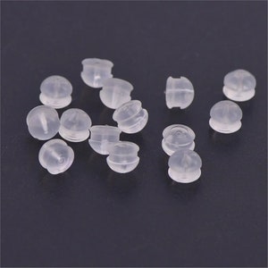 May include: A group of small, clear, plastic earring backs. The backs are round with a small hole in the center.