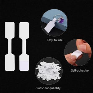May include: White self-adhesive price tags with a loop for hanging. The tags are easy to use and come in a sufficient quantity.  The image shows a tag attached to a ring with a purple gemstone.