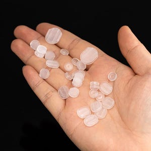 Peut inclure: Une main tenant une variété de petits embouts d'écouteurs en plastique transparent. Les embouts sont de différentes tailles et formes.