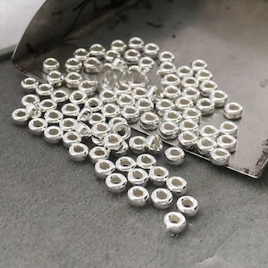 Puede incluir: Una gran cantidad de anillos de salto de metal plateado. Los anillos son pequeños y redondos con un agujero en el centro. Están dispersos sobre una superficie gris.