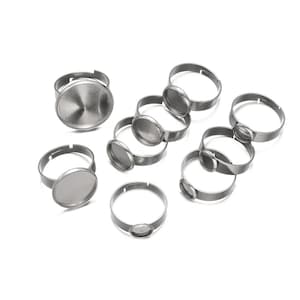 May include: A set of ten silver-toned metal rings with round, flat, bezel-set settings. The rings are designed for crafting jewelry and are ideal for adding a personal touch to your creations.