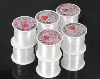 Könnte beinhalten: Sechs Spulen mit klarem elastischem Garn, jede mit einem roten und weißen Etikett mit der Aufschrift "Strong & Stretchy" und "0.50".
