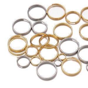 Op de afbeelding: Assortiment van zilveren en gouden sleutelringen in verschillende maten. De sleutelringen zijn willekeurig gerangschikt op een witte achtergrond.