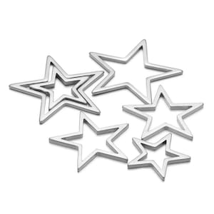 Puede incluir: Un conjunto de seis abalorios de metal plateado en forma de estrella de diferentes tamaños. Los abalorios están todos abiertos y tienen un acabado liso y pulido.