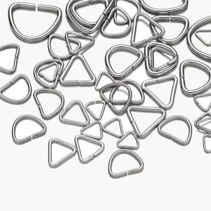 Könnte beinhalten: Eine Sammlung von silberfarbenen Metallringen und dreieckigen Formen. Die Formen sind in verschiedenen Größen und auf einem weißen Hintergrund verstreut. Die Ringe sind D-förmig und die Dreiecke sind gleichseitig.