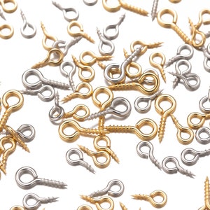 Może przedstawiać: Zbliżenie na różne złote i srebrne śruby z oczkiem. Śruby są rozrzucone na białym tle.