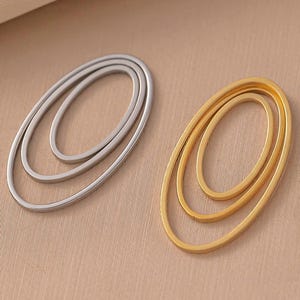 Könnte beinhalten: Zwei Paar ovale Ohrringe, ein Paar ist silberfarben und das andere goldfarben. Jeder Ohrring besteht aus drei konzentrischen Ovalen.