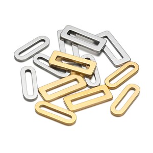 Könnte beinhalten: Eine Gruppe von goldenen und silbernen Metall-Sprühringen. Die Sprühringe sind oval und rechteckig geformt. Sie werden für die Schmuckherstellung verwendet.