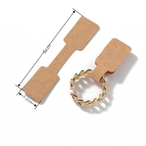 May include: Two brown paper tags with a gold chain ring attached. The larger tag measures 6 inches by 1.2 inches. The smaller tag measures 1.2 inches by 1.2 inches.