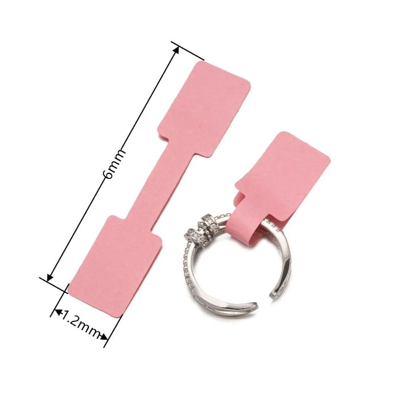 May include: Two pink paper tags with a rectangular shape and a narrow strip for attaching to a product. The tags are 1.2 inches wide and 6 inches long.
