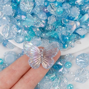 Peut inclure: Assortiment de breloques en plastique bleu irisé de différentes formes, notamment des papillons, des coquillages, des fleurs et des nœuds. Les breloques sont parfaites pour ajouter une touche de fantaisie à vos bijoux, vos créations et autres projets.