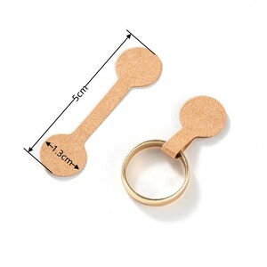 May include: Two brown paper ring sizing tags with a 1.3 inch diameter circle on each end and a 5 inch long strip connecting the circles. The tags are designed to be used for sizing rings.