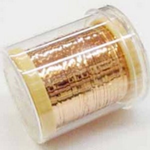 Puede incluir: Un recipiente de plástico transparente que contiene una bobina de alambre de color cobre. El alambre está enrollado firmemente y parece estar hecho de hebras finas y planas. El recipiente tiene una tapa transparente y una etiqueta amarilla.