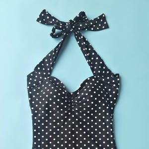 May include: A black and white polka dot swimsuit with a halter neck and a gathered bust. The swimsuit has a high leg cut and a low back.