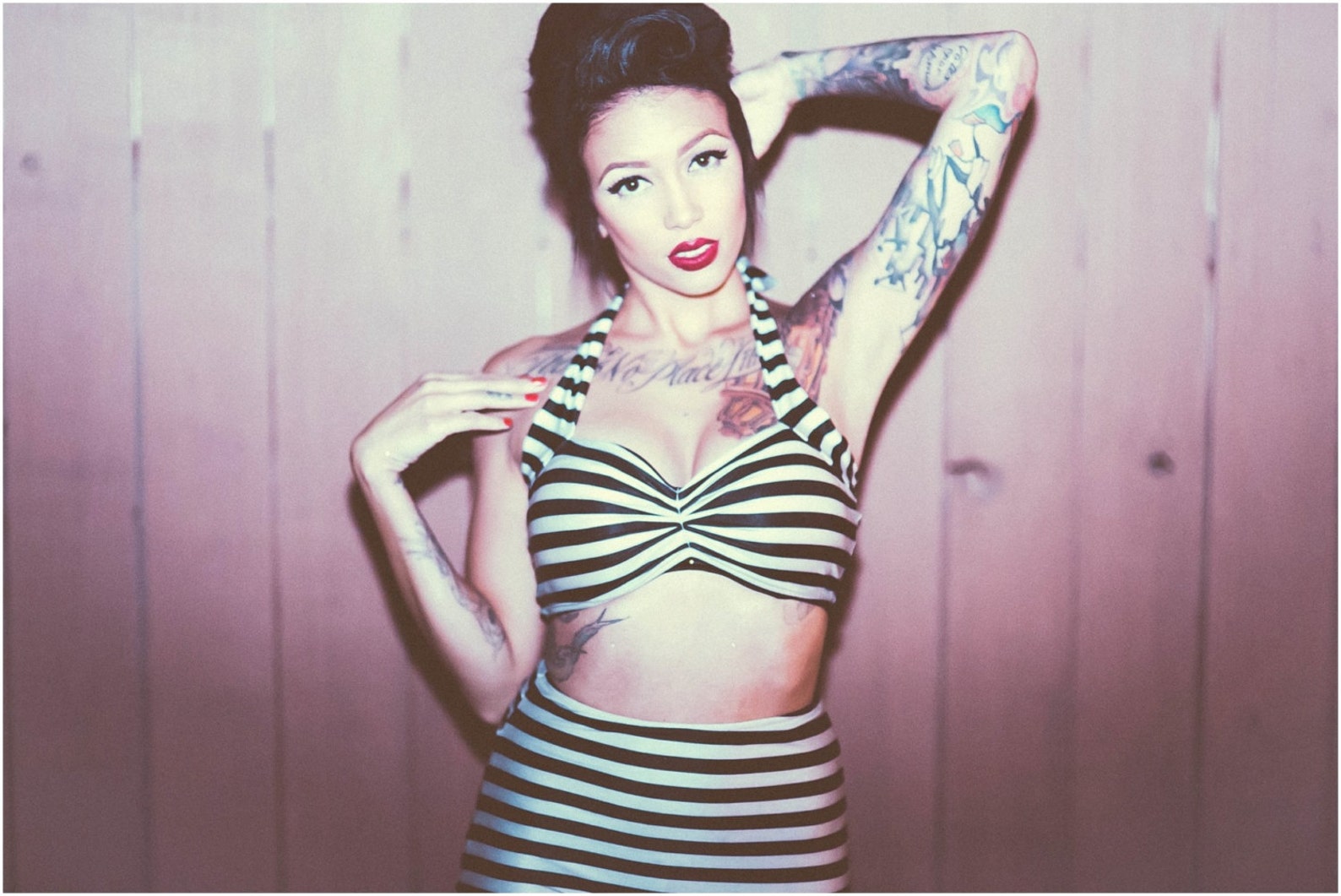 Tattooed woman in pin-up style wearing a retro goth bikini with black and white stripes, halter top, and high-waisted bottoms.