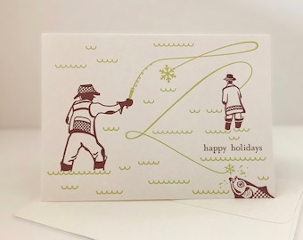 May include: Holiday greeting card featuring a brown illustration of two people fishing in a snowy scene. The words "happy holidays" are printed in brown. A fish jumps out of the water. The card is on a white background.