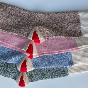 Puede incluir: Cuatro pares de calcetines de diferentes colores: marr&oacute;n, rosa, azul y verde. Cada calcet&iacute;n tiene un pu&ntilde;o blanco y un ribete rojo en la punta.