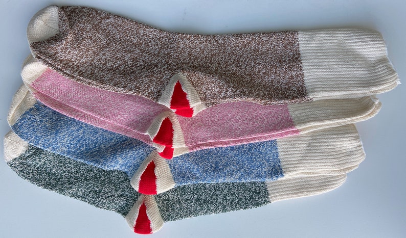 Puede incluir: Cuatro pares de calcetines de diferentes colores: marr&oacute;n, rosa, azul y verde. Cada calcet&iacute;n tiene un pu&ntilde;o blanco y un ribete rojo en la punta.