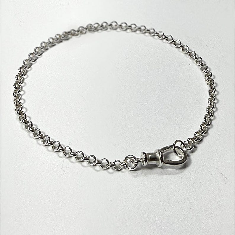 May include: A silver-toned chain bracelet featuring a series of uniform circular links connected in a continuous loop. The bracelet is secured with a polished metal lobster claw clasp that connects to a small jump ring, creating a simple design.