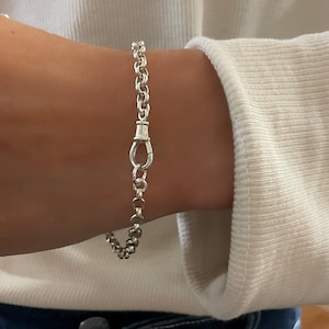 May include: A silver chain bracelet featuring round, interlocking links and a central swivel clasp mechanism. The bracelet is constructed from polished metallic silver, showcasing a uniform link pattern that connects to a functional, secure lobster-style swivel clasp closure.
