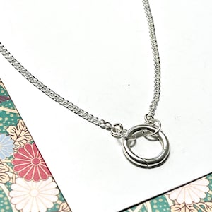 Puede incluir: Un collar de cadena de plata con un simple colgante de anillo de plata.