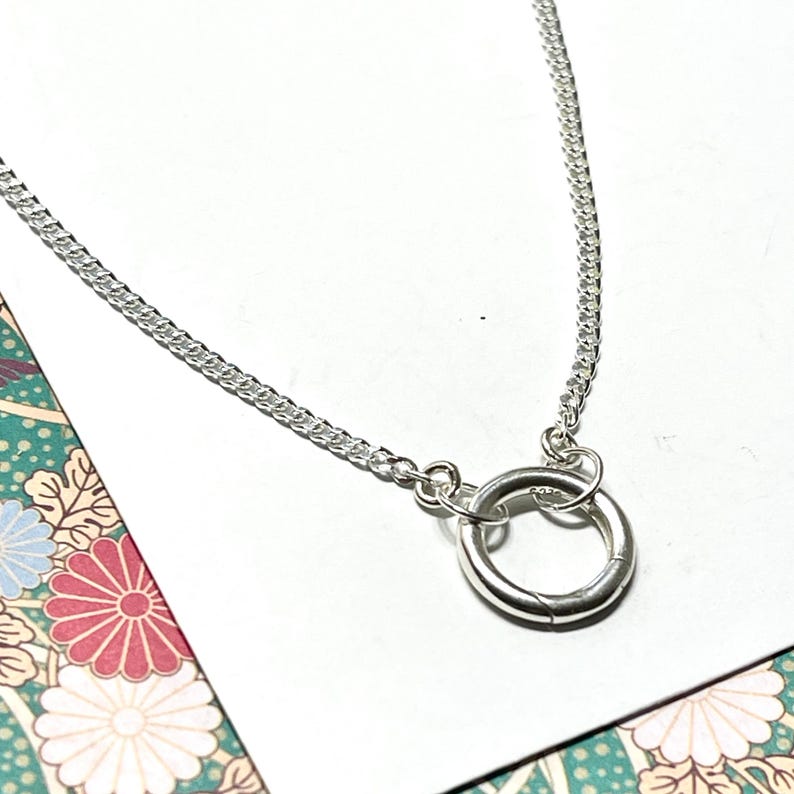 Puede incluir: Un collar de cadena de plata con un simple colgante de anillo de plata.