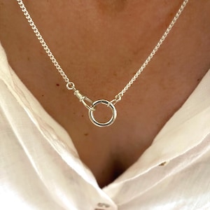 Peut inclure: Un collier à chaîne argentée doté d'un fermoir à anneau circulaire et d'un connecteur pivotant. Les maillons métalliques sont petits et uniformes, créant une apparence délicate. Le collier est placé autour du cou, mettant en valeur la finition.