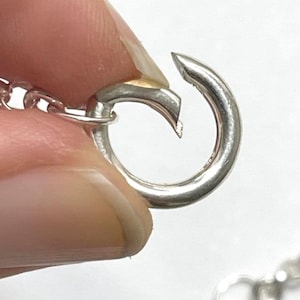 Puede incluir: Primer plano de un cierre plateado para un collar o pulsera. El cierre est&aacute; abierto y listo para ser unido a una cadena.