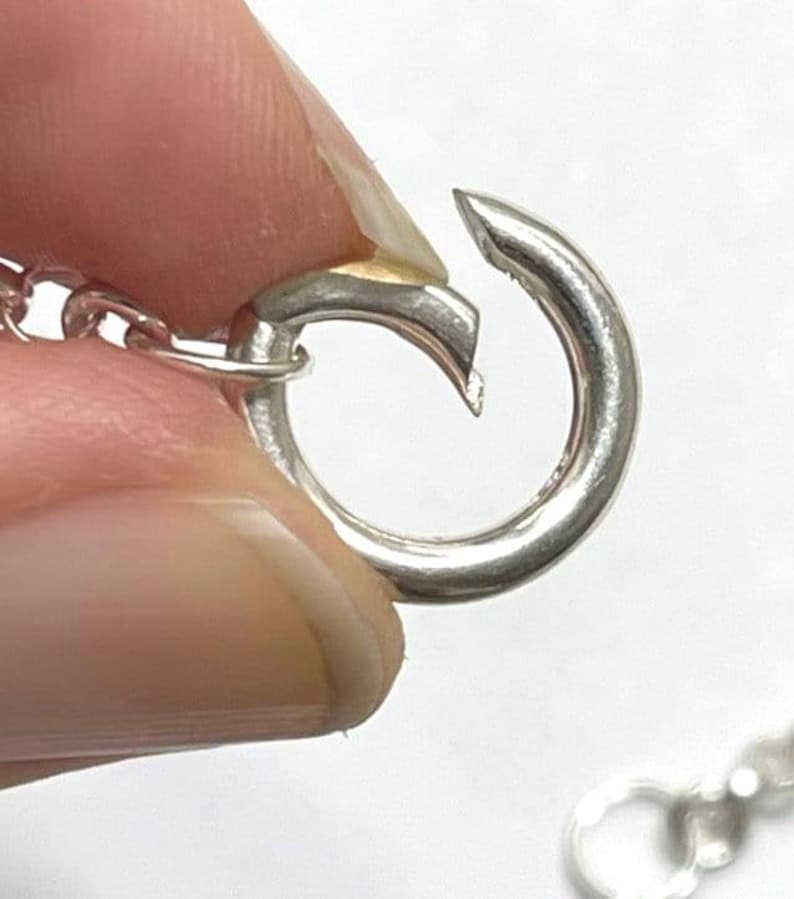 Puede incluir: Primer plano de un cierre plateado para un collar o pulsera. El cierre est&aacute; abierto y listo para ser unido a una cadena.