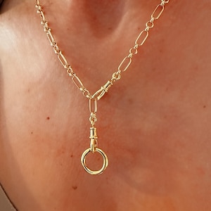 May include: A gold-toned necklace featuring a chain with elongated oval links. The necklace includes a central vertical drop section that connects to a circular ring pendant via a small, functional-style swivel clasp mechanism.