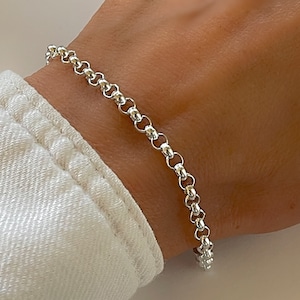 May include: A silver chain bracelet featuring a series of interconnected round, polished links. The bracelet is constructed with a classic rolo chain design, showcasing a bright, reflective metallic finish that wraps around the wrist area.