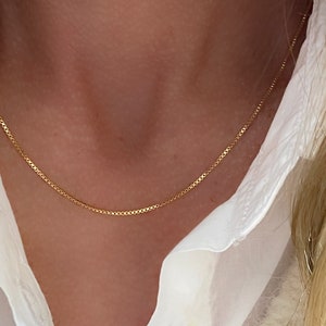 May include: A delicate gold chain necklace worn on a person's neck. The chain is thin and has a simple design.