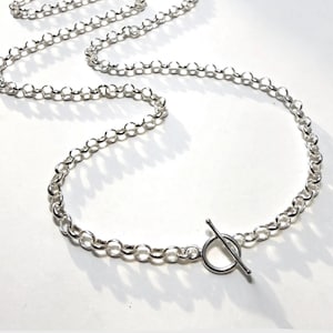 May include: A silver-colored necklace with a toggle clasp. The chain is made of small, round links. The toggle clasp is a simple design with a circular ring and a straight bar. The necklace is displayed on a white surface.