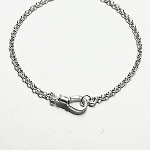 May include: A silver-colored chain bracelet featuring a polished, teardrop-shaped clasp mechanism. The bracelet is constructed from a series of small, uniform circular links that connect to the central fastener, creating a continuous loop design.
