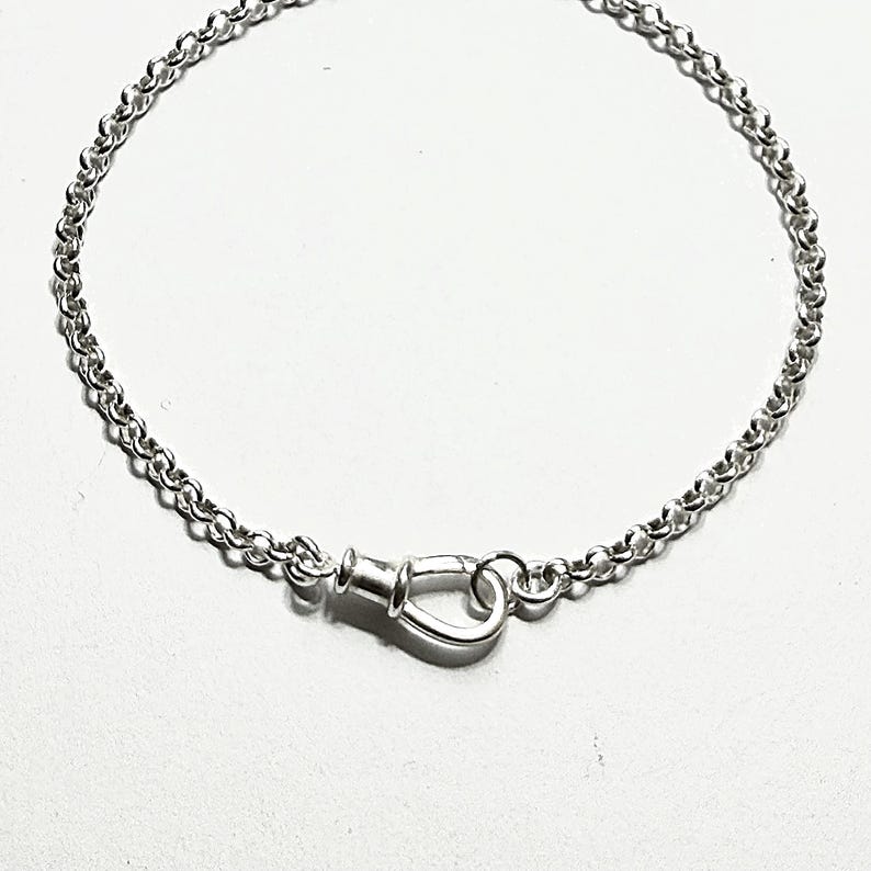 May include: A silver-colored chain bracelet featuring a polished, teardrop-shaped clasp mechanism. The bracelet is constructed from a series of small, uniform circular links that connect to the central fastener, creating a continuous loop design.